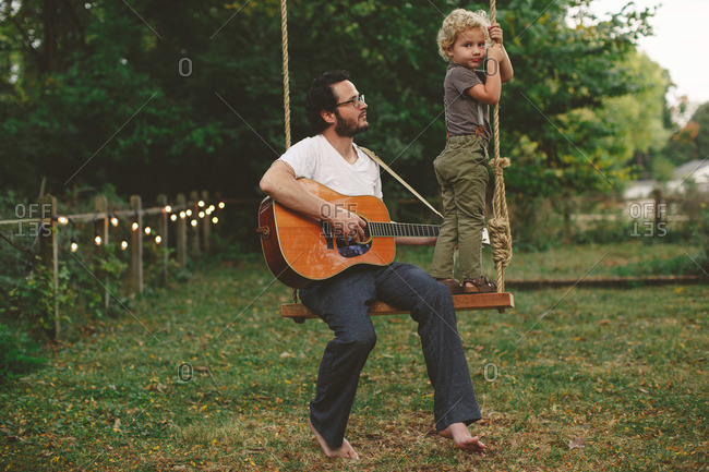 Dad playing guitar for his son while sitting on a swing