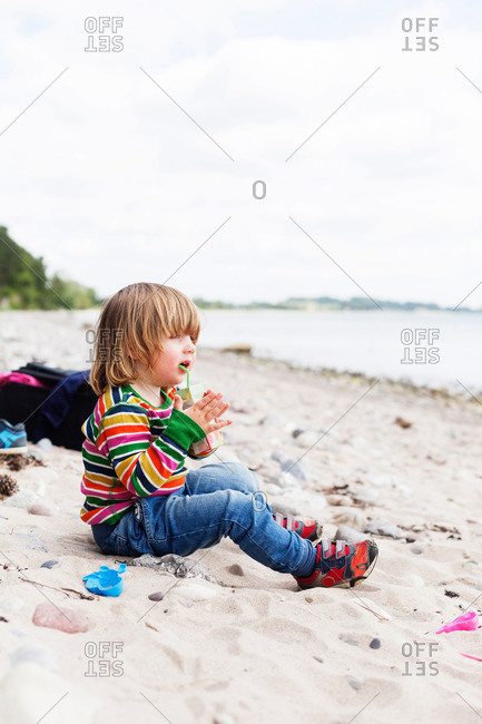 Toddler girl in striped shirt drinking a juice box on beach