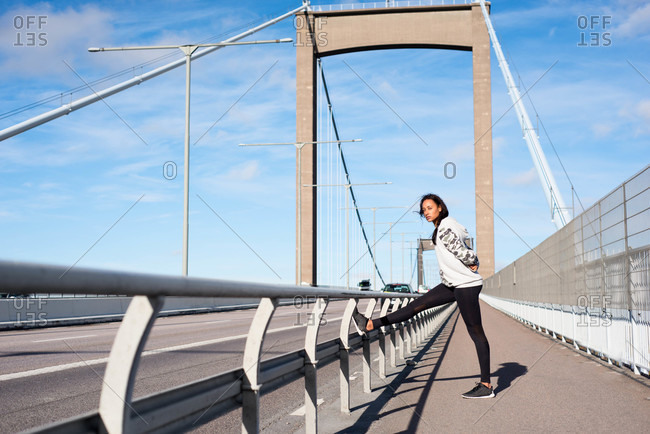 Runner stretching against a railing on a bridge