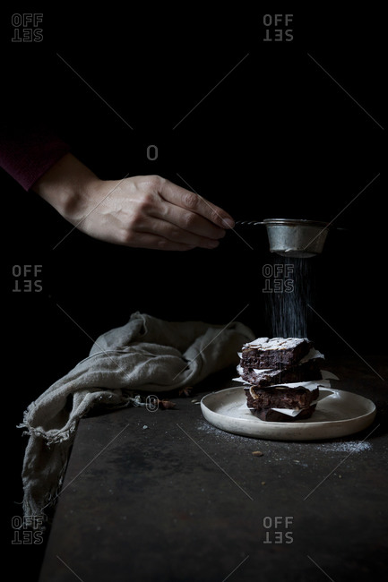 Sifting powdered sugar onto a stack of chocolate vegan brownies