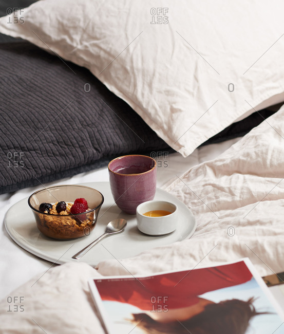Breakfast tray of granola on a bed with bedding and pillows