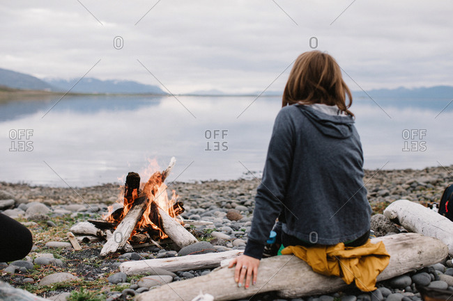 Woman sitting by a campfire looking at a lake, Laugavegur Trail, Iceland