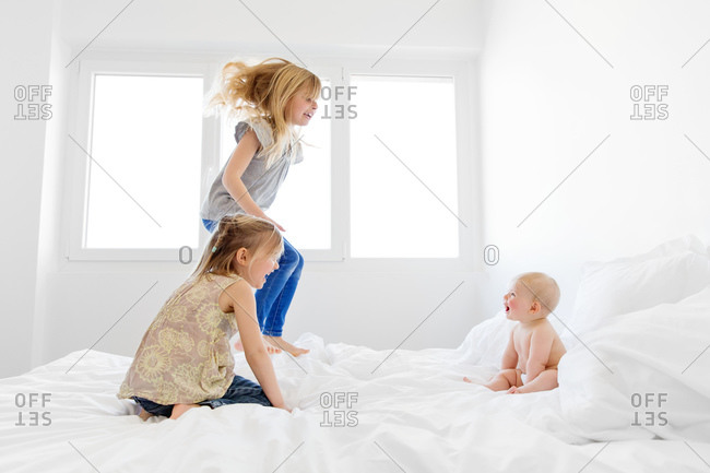 Sisters jump on bed while baby watches