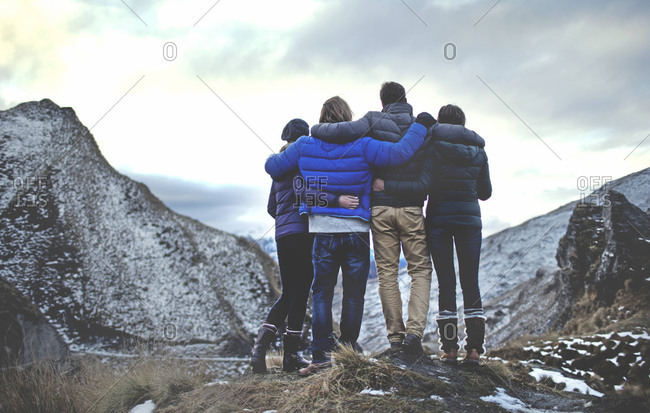 Four friends with arms around each other stand on edge of cliff