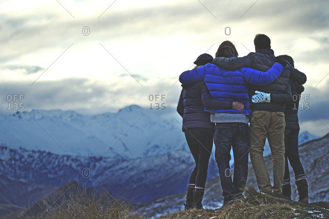 Four affectionate friends stand at mountain\'s edge with arms around each other
