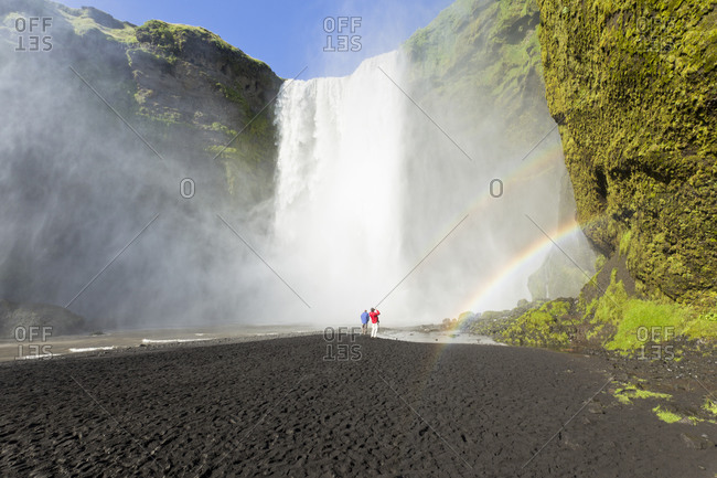Tourists and rainbow at Icelandic waterfall