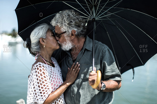 Affectionate senior couple kissing under umbrella