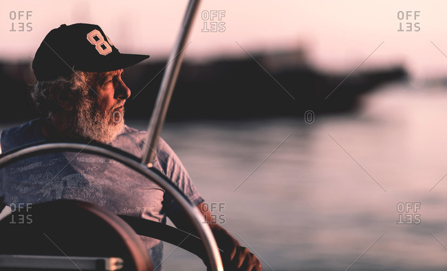 Senior man driving a boat at sunset