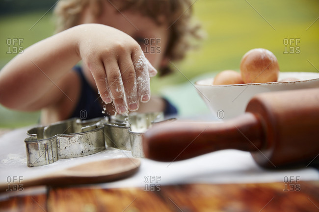 Boy sprinkling flour on cookie cutouts