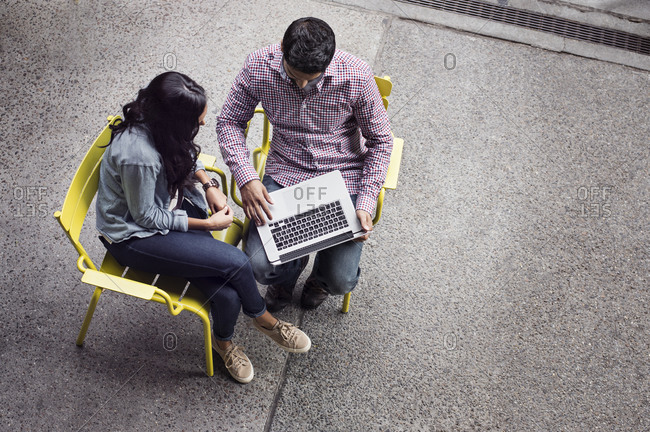 Elevated view of man and woman seated in yellow chairs using laptop computer outside