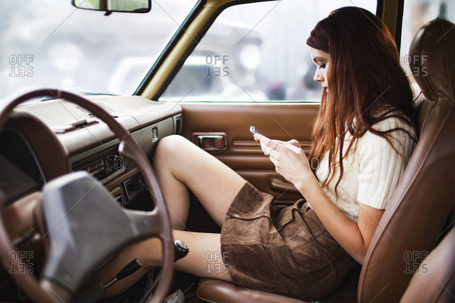 Woman in front seat of vintage automobile uses her smartphone