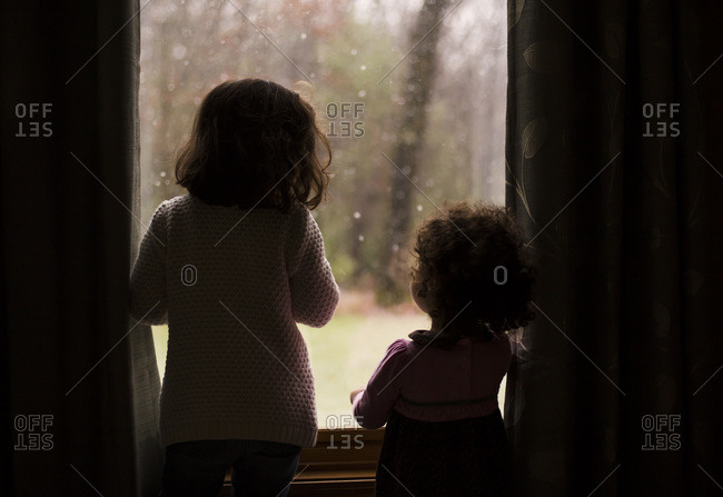Two little girls looking out a window watching snow fall
