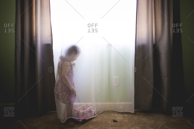 Little girl playing with toys behind a sheer curtain