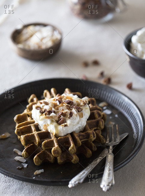 Elevated view of pumpkin waffles topped with coconut whipped cream, pecans, and maple syrup