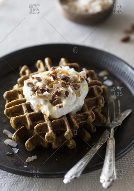 Pumpkin waffles topped with coconut whipped cream, pecans, and maple syrup
