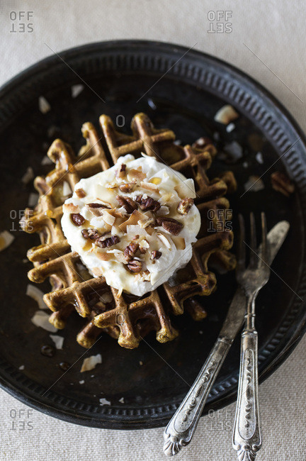 Overhead view of pumpkin waffles topped with coconut whipped cream, pecans, and maple syrup
