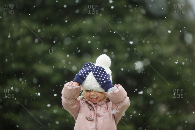 Happy young girl in polka dot mittens fixes her hat during snowfall