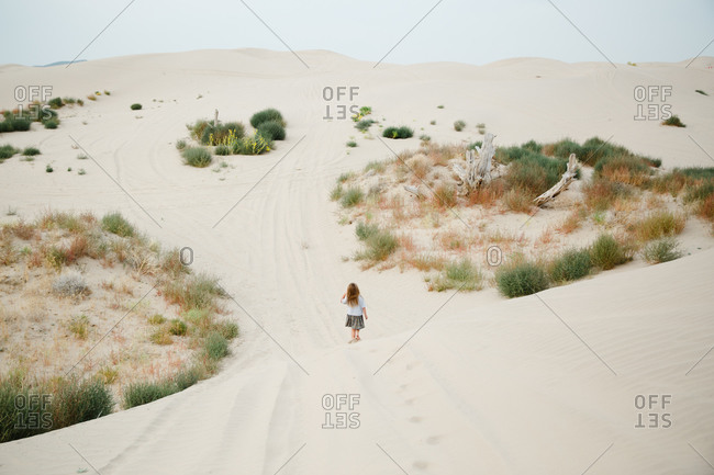 Young girl walking past brush in sand dunes