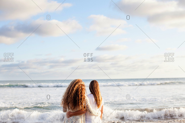Back view of mother and daughter standing with arms around each other on beach