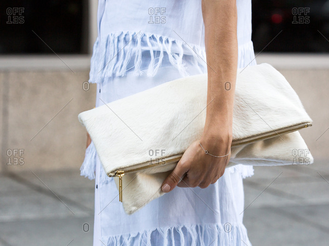 Woman in a fringed outfit holding a linen clutch