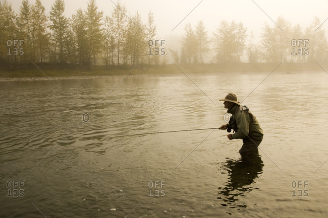 A man fly-fishing on Elk River, BC, Canada on a misty morning