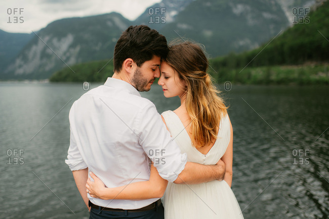 Newlyweds standing with arms around each other in front of a lake