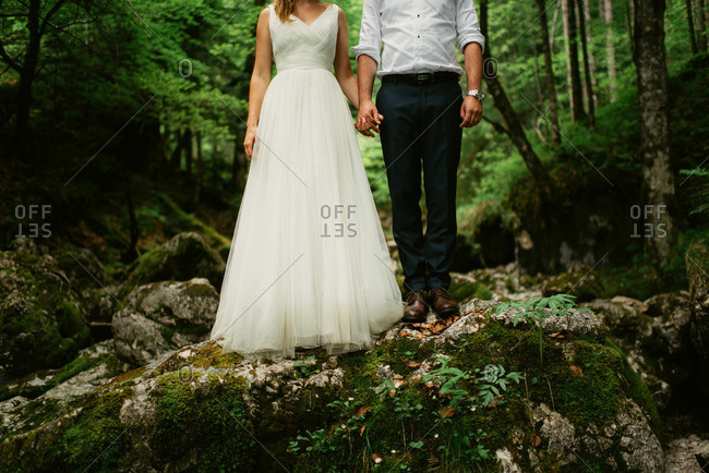 Bride and groom standing on a large rock in the woods