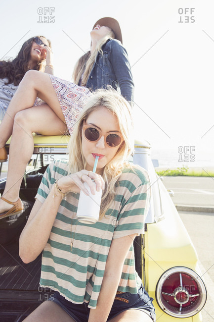 Young woman sipping soda on the back of a car with her friends