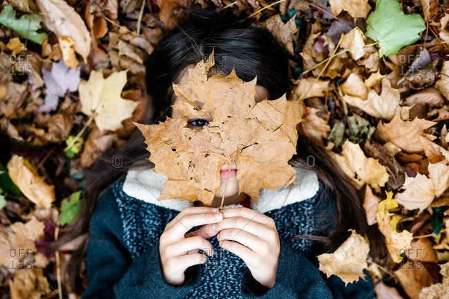 Little girl lying in fallen leaves with one covering her face