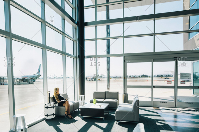 A beautiful lady sits on a sofa in a large glass fitted airport terminal
