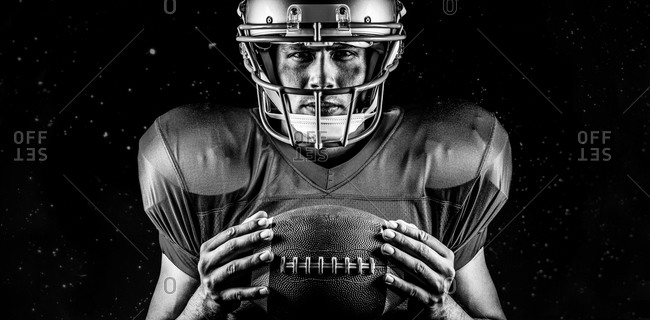 Close-up portrait of confident American football player holding ball against black background