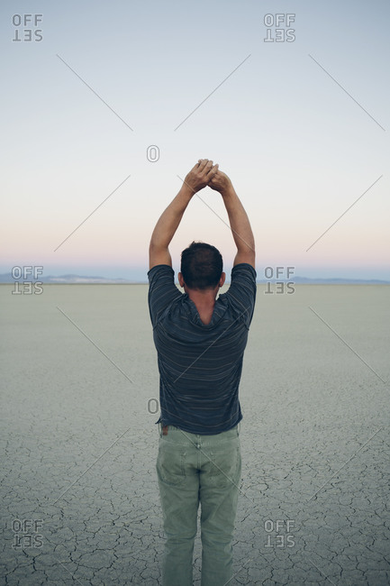 Man stretching with arms above head, facing the sunrise over expansive desert, Black Rock Desert, Nevada