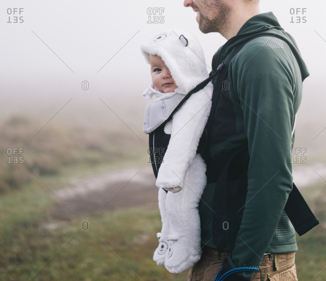 A man carrying a baby in a baby carrier on his chest, outdoors on a misty autumn day