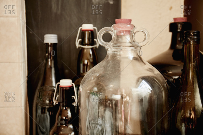 A shelf of bottles and jars, one large double handled jar with a stopper and bottles with lids