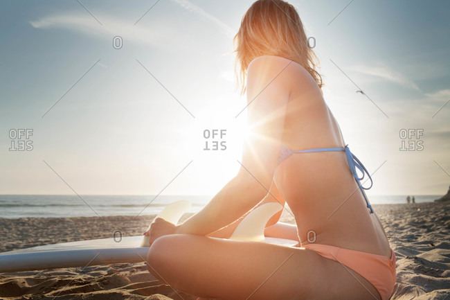 Woman on sun dappled beach with surfboard