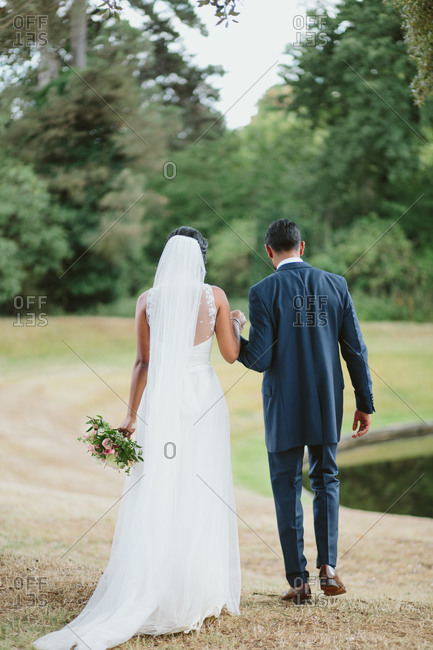Back view of bride and groom walking toward a pond
