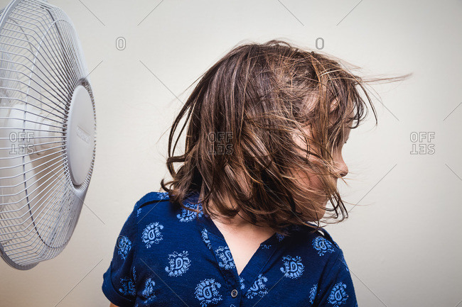 Cute young girl turning her head to enjoy breeze from fan