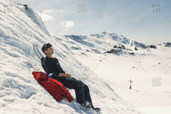 Side view of man with skis relaxing on steep snow hill