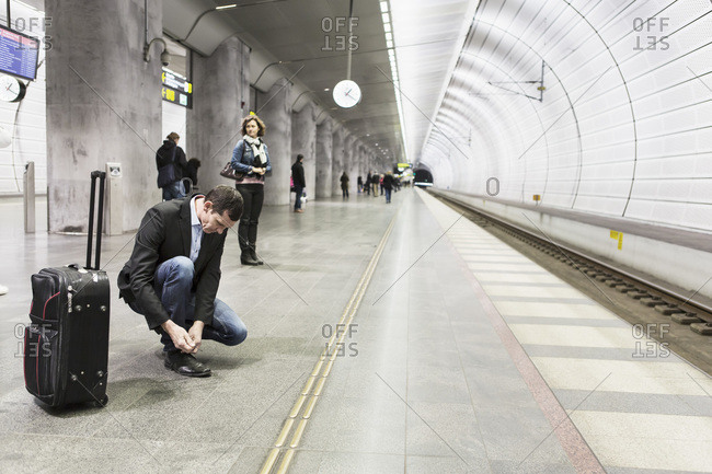 Businessman tying shoelace while waiting at railway station