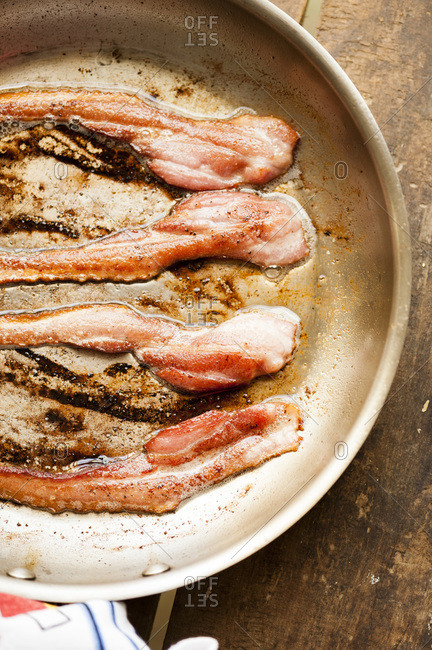 Strips of bacon in skillet on wooden table