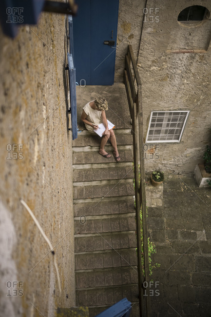 Woman sitting on stairs of a house drawing a picture