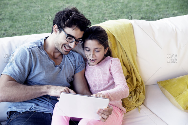 Girl and dad with tablet on outdoor couch