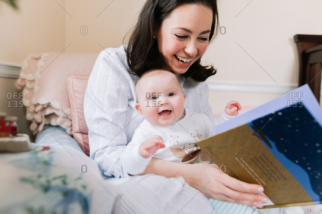 Mother and baby daughter smiling as they read a story book together