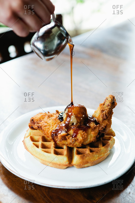 Syrup being poured over fried chicken and waffles