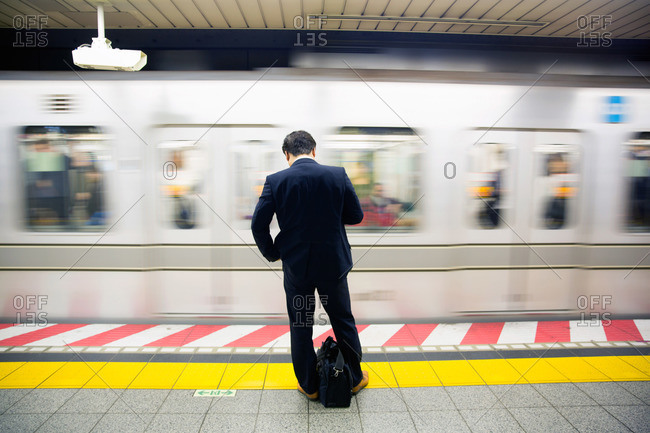 Man using smartphone while waiting in subway station, Tokyo, Japan