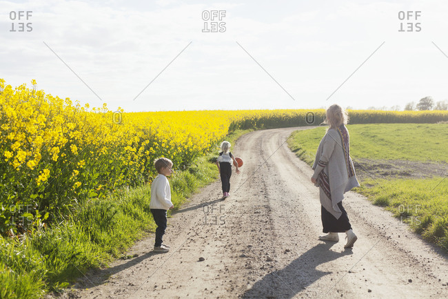 Mother and children playing with a ball on a road by yellow flowers