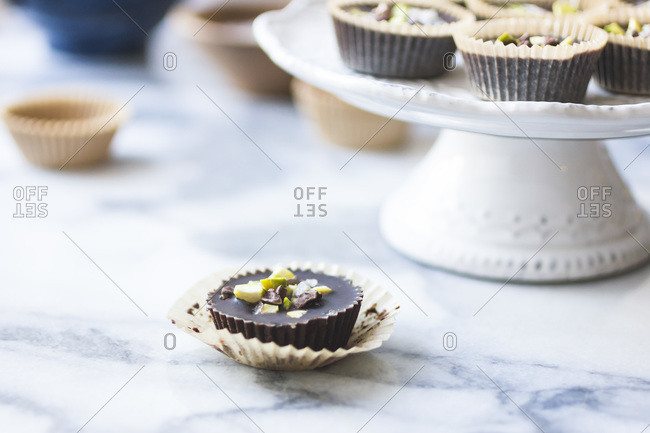Chocolate pistachio butter cups on marble surface and cake stand