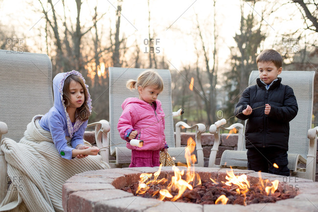Three children roasting marshmallows over outdoor gas fireplace