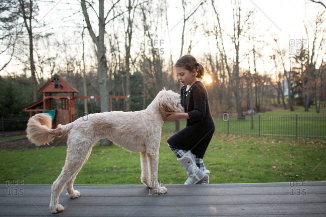Young girl greeting her dog on backyard deck at sunset