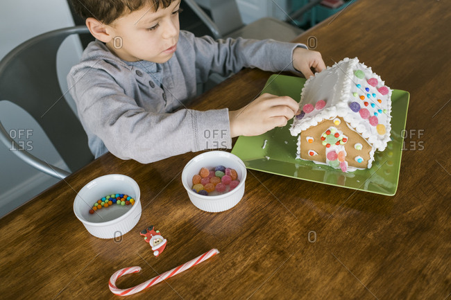 Boy putting gum drops on the roof of a gingerbread house